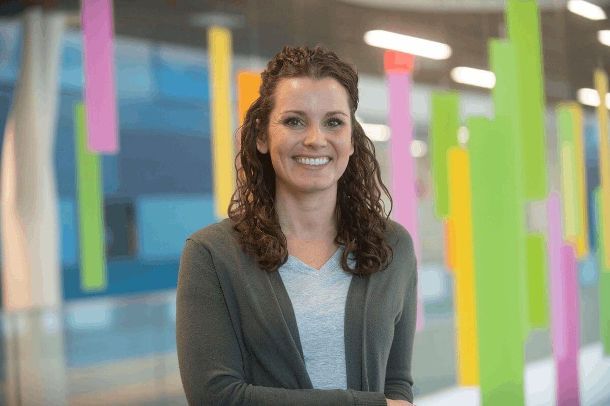 Woman with curly brown hair smiling at camera in modern office with colorful vertical panels in background