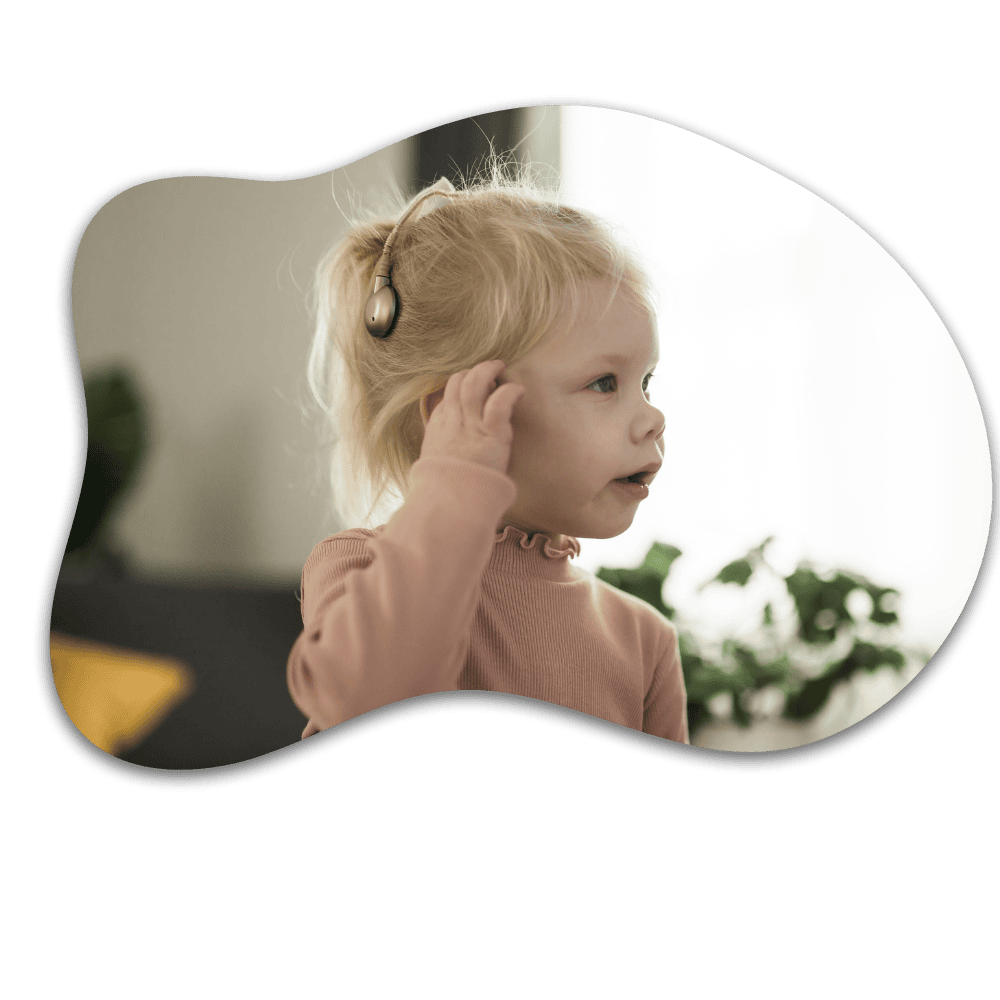 Young child with blonde hair wearing headphones and a pink sweater, listening to audio with hand near ear in an indoor setting