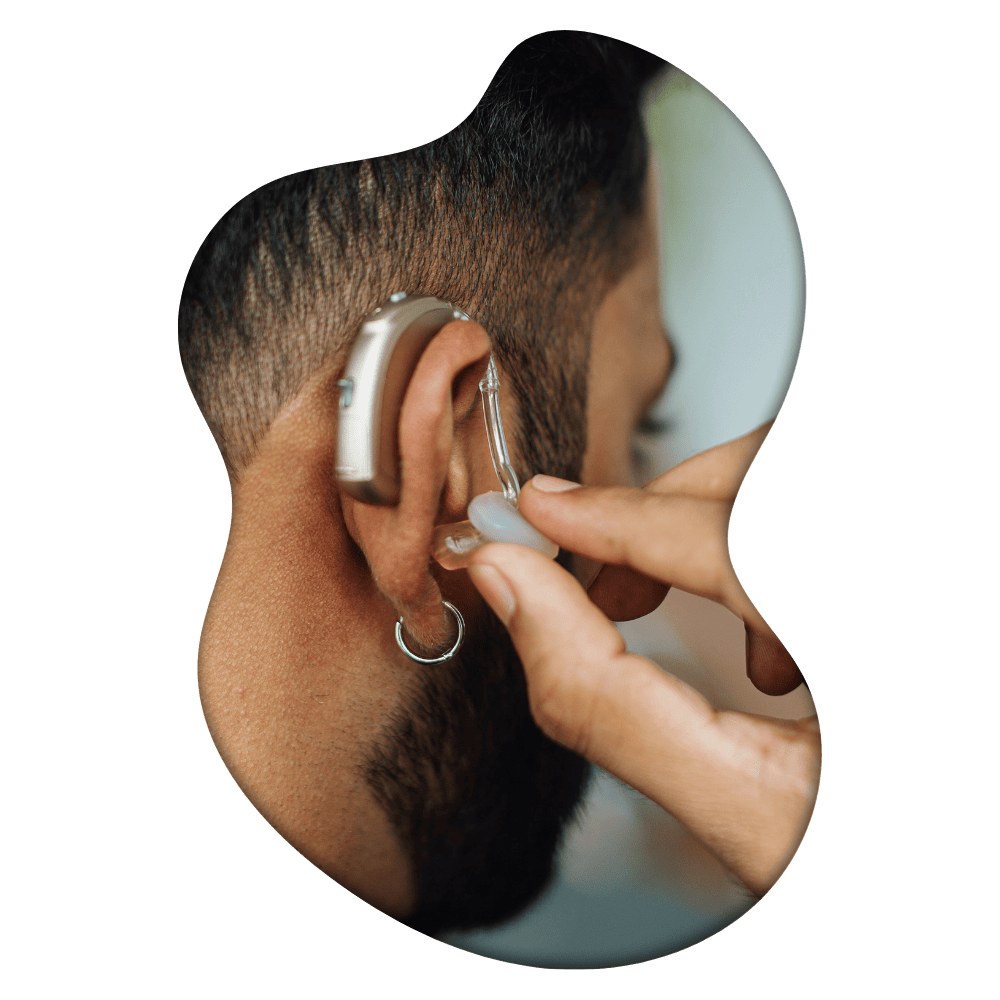 Close-up of a hearing aid being inserted into a person's ear by another person's hands