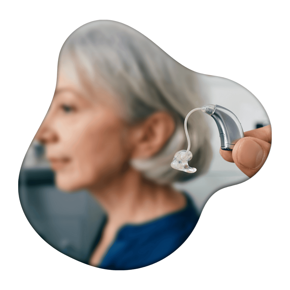 Woman with gray hair wearing a behind-the-ear hearing aid, shown in profile with a hand holding the device visible