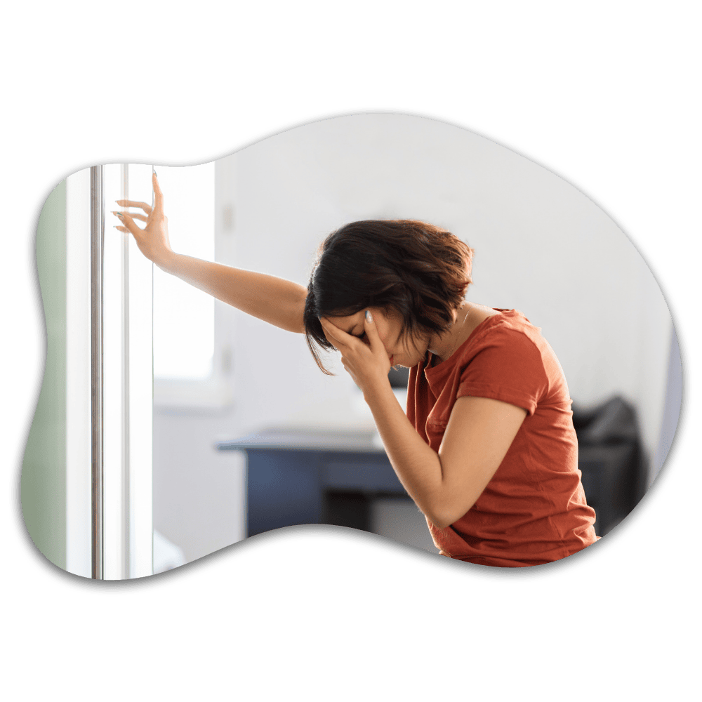 Woman in red shirt leaning against window with hand to face, appearing stressed or thoughtful in modern office setting