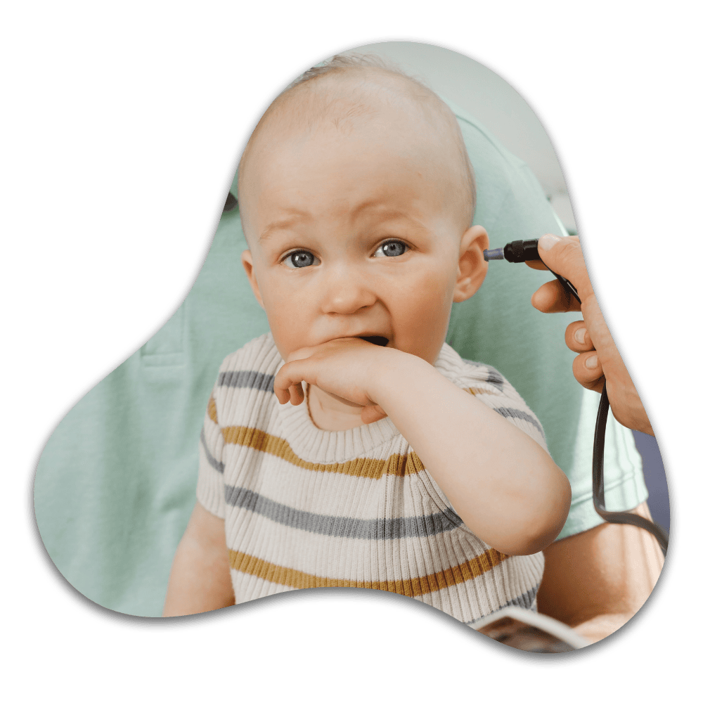 Infant with hand in mouth wearing striped shirt, held by person with stethoscope during medical examination