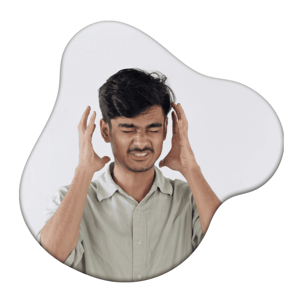 Man in beige shirt holding his head with hands closed eyes and grimacing expression against white background