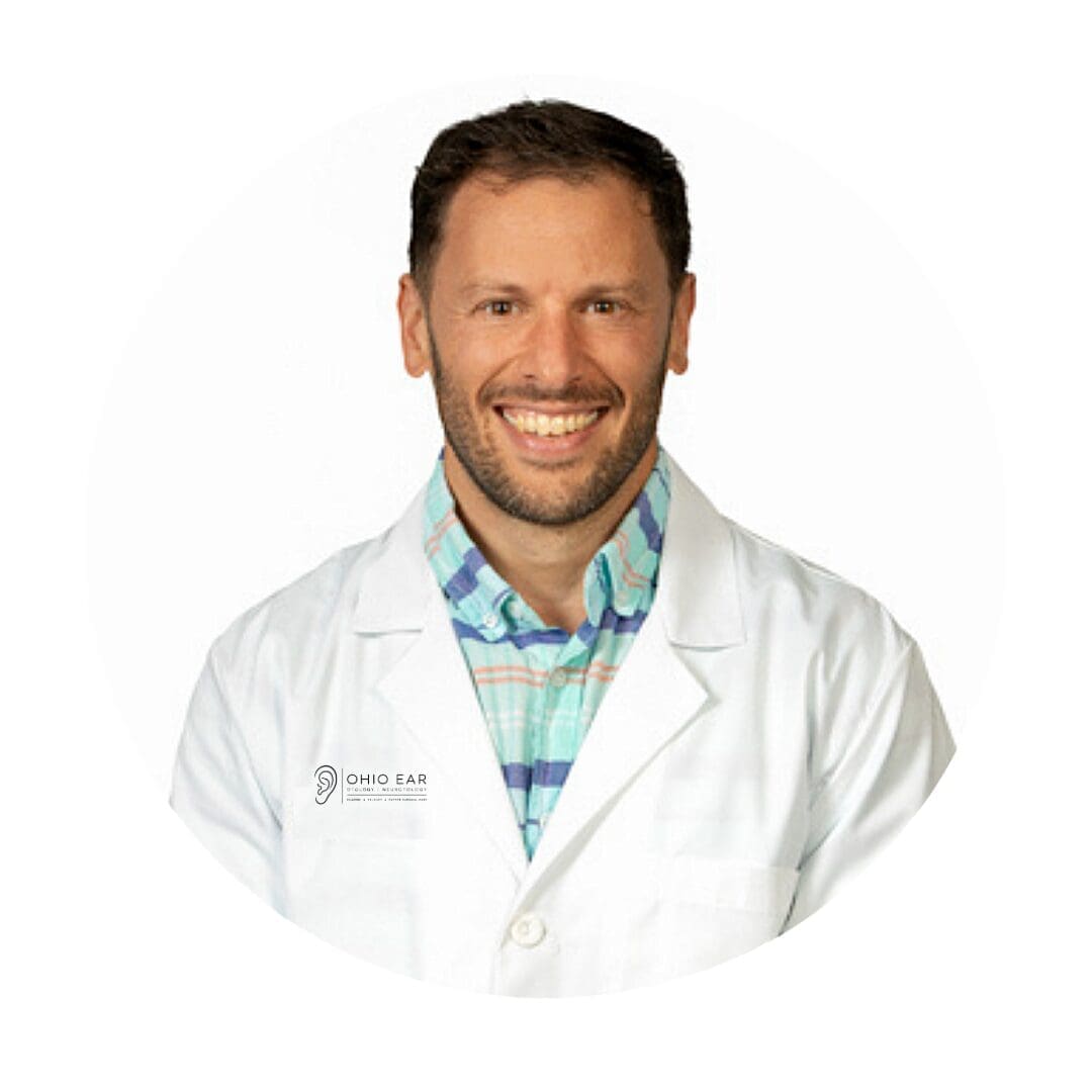 Professional headshot of a smiling male doctor wearing a white lab coat over a teal patterned shirt, affiliated with Ohio Ear