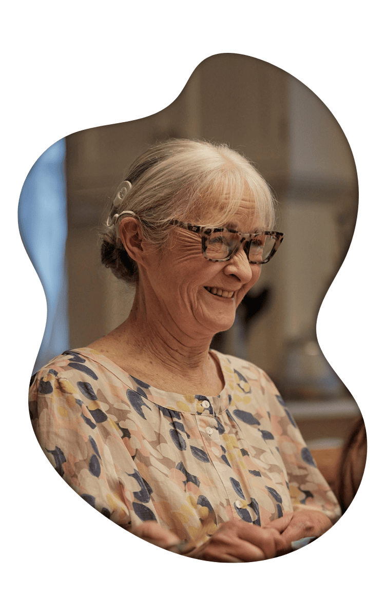 Smiling woman with white hair and tortoiseshell glasses wearing a patterned beige and navy blouse